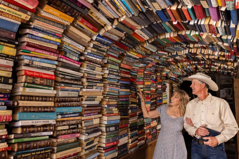 Couple walking through the book tunnel at Intermission Bookshop. The woman is reaching up to touch a book.